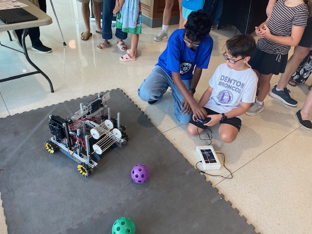 Techs Mechs member helping a visitor drive the robot at the Texas 4-H Open House